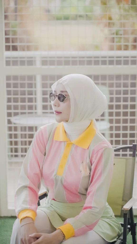 wanita berpose di latar belakang jaring,melihat jauh pakaian santai padel, topi, dan tas tenis.
