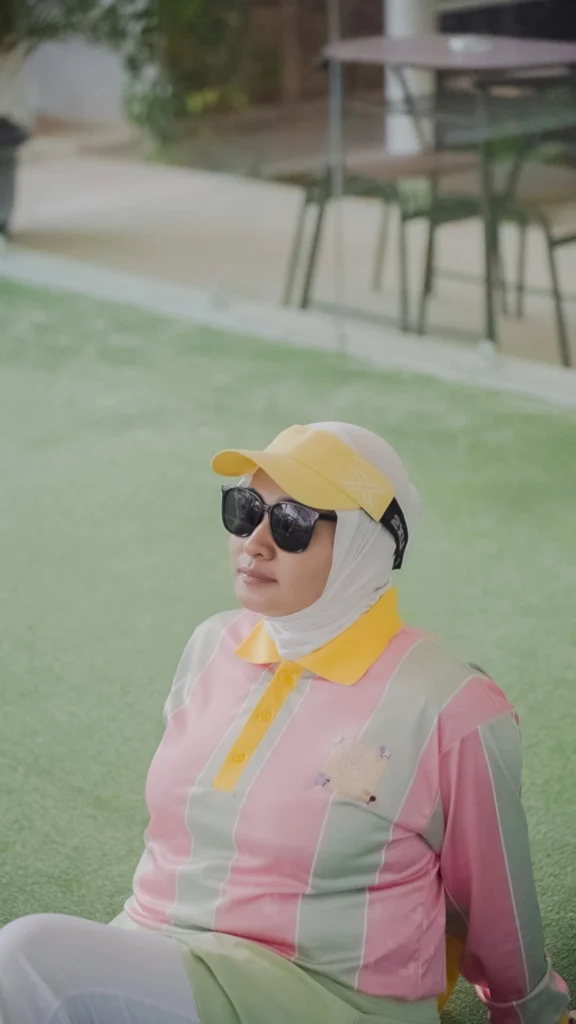 wanita duduk sebelum main padel dengan kacamata dan topi dan kerudung