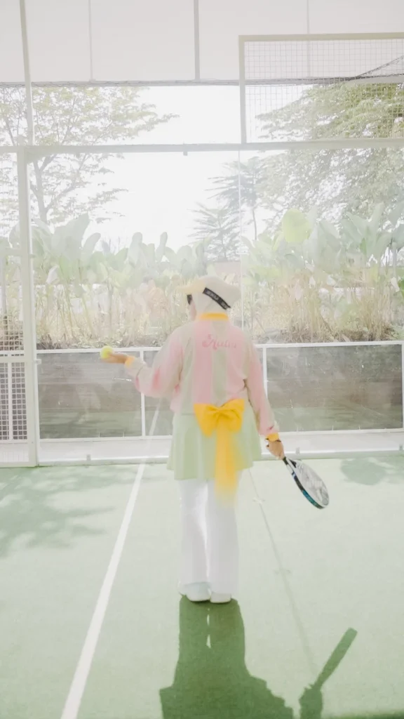 wanita main padel berpose dengan baju estetik warna pastel, tenis di lapangan.