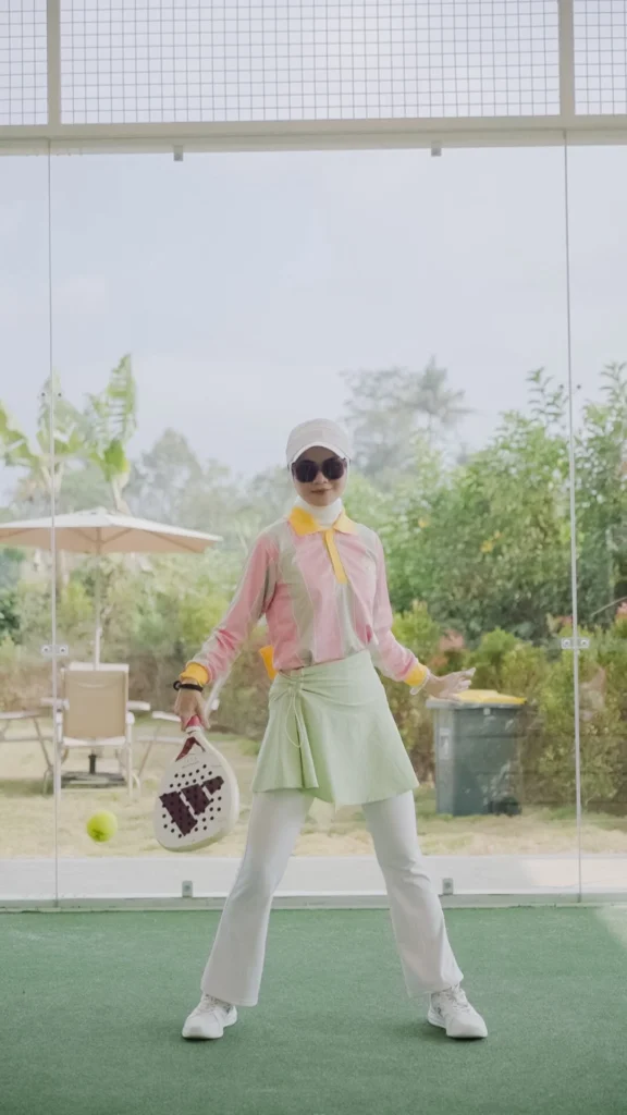wanita bermain padel berpose dengan raket padel, pakaian modern, latar belakang taman.