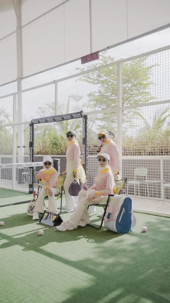 wanita bermain padel dalam pakaian seragam, berpose di lapangan padel, latar belakang taman hijau.