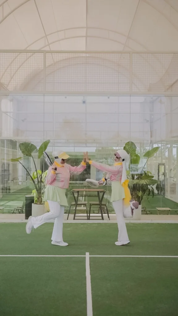 wanita bermain berpose tos di lapangan tenis, pakaian formal, latar belakang ruang terbuka.