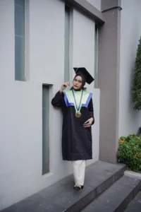Aila Stikes Purwokerto Aston, seorang wanita dalam pakaian sarjana yang menatap dinding.