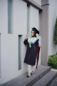 Aila Stikes Purwokerto Aston dalam foto wisudanya sedang berdiri di dinding.