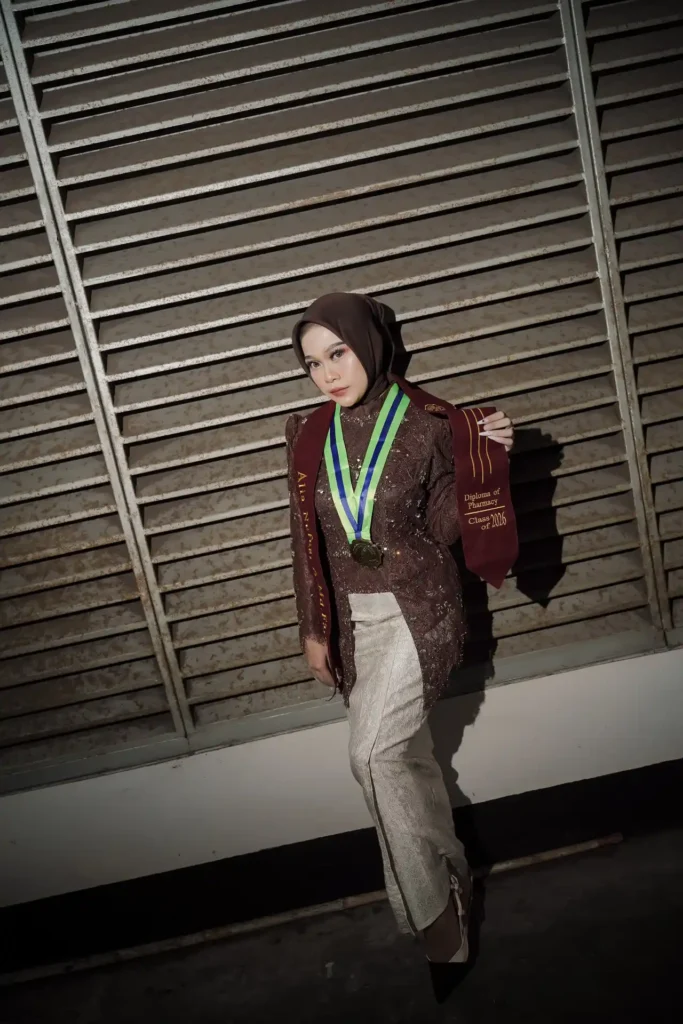 Aila Stikes Purwokerto Aston dalam acara wisuda, wanita tersebut sedang berpose dengan medali di lehernya.