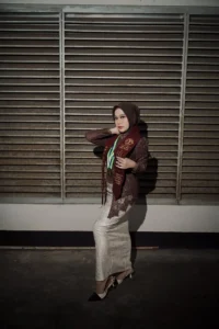 Aila Stikes Purwokerto Aston, seorang wanita berhijab yang berdiri tegak dengan tangan di pinggang, mengambil foto wisuda.