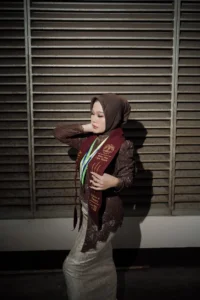 Aila Stikes Purwokerto Aston dalam foto wisuda, wanita dalam pakaian sarjana berdiri dengan tangan di pinggang.
