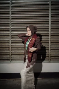 Aila Stikes Purwokerto Aston dalam foto wisudanya sedang berdiri dalam keceriaan, memakai pakaian sarjana.