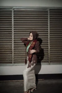 Aila Stikes Purwokerto Aston: Seorang wanita berpakaian jas merah berdiri dengan tangan di pinggangnya.