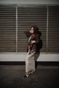 Aila stikes Purwokerto Aston sedang berfoto wisuda dengan penampilan elegan dalam sehelai dress, sementara tangannya diletakkan di pinggang dan kaki.