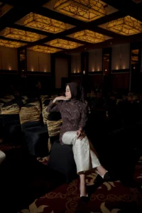 Aila, seorang mahasiswa Stikes Purwokerto Aston, sedang duduk di kursi dan memamerkan dirinya dalam foto wisuda, menampilkan pakaian hitam dan putih.