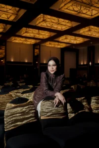 Aila Stikes Purwokerto Aston wisuda di kamar dengan lantai berpola cekker hitam dan putih.