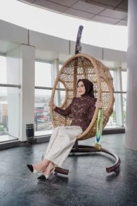 Aila Stikes Purwokerto Aston sedang duduk di kursi wicker.