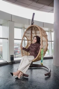 Aila Stikes Purwokerto Aston sedang duduk di kursi wicker.