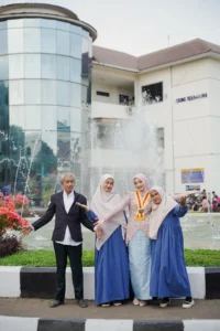 Kristina UMP, Universitas Muhammadiyah Purwokerto, sedang berpose di depan sebuah fountain dengan dua orang lainnya, sementara sebuah gedung terlihat di latar belakang.