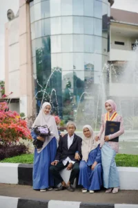 Seorang wanita dalam pakaian biru dan seorang pria dalam pakaian putih berdiri di depan sebuah fonsai, mengambil foto untuk wisuda di Universitas Muhammadiyah Purwokerto.