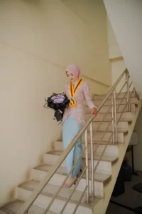 Kristina UMP, seorang wanita berpakaian biru yang membawa bunga, berdiri di atas tangga.