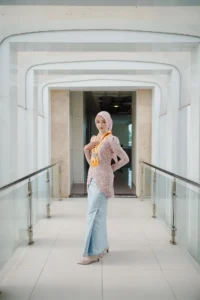 Seorang wanita berpakaian merah dan biru berdiri di lorong, membawa telepon, setelah wisuda di Universitas Muhammadiyah Purwokerto.