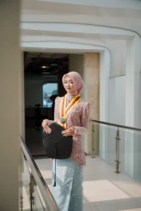 Krisnika UMP, seorang wanita berpakaian biru yang membawa tas hitam, berdiri di depan gedung universitas.