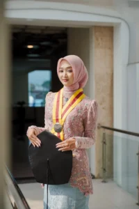 Kristina, mahasiswa Universitas Muhammadiyah Purwokerto, memenangkan medali merah sambil membawa folder hitam di depan gedung.