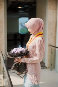 Kristina UMP, seorang wanita berpakaian merah yang membawa bunga, berdiri di depan bangunan Universitas Muhammadiyah Purwokerto.
