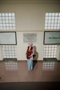 Kristina UMP universitas Muhammadiyah Purwokerto sedang berdiri di depan gedung, memakai pakaian merah dan putih, dan tampaknya sedang melihat ke kamera.