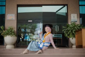 Kristina UMP, seorang wanita yang memakai dress merah dan headscarf biru, berpose di depan gedung universitas.
