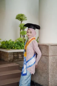 Kristina dari Universitas Muhammadiyah Purwokerto sedang berpose dalam pakaian wisuda.