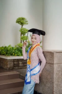 Kristina, seorang mahasiswa Universitas Muhammadiyah Purwokerto, sedang memamerkan gelar akademinya dalam foto wisuda.