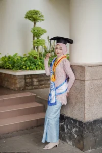 Kristina UMP, seorang mahasiswa Universitas Muhammadiyah Purwokerto, sedang berdiri di jalan raya, memakai cap dan gowns wisuda, dan mengambil foto.