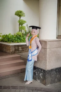 Kristina, seorang mahasiswa Universitas Muhammadiyah Purwokerto, sedang berdiri di jalanan dengan pakaian sarjana.
