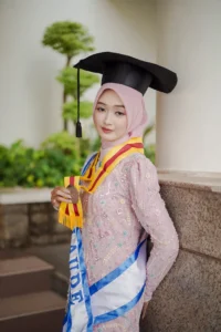Kristina dari Universitas Muhammadiyah Purwokerto dalam foto wisuda dengan pakaian sarjana yang sedang berpose.