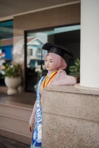 Seorang wanita dalam pakaian sarjana sedang menunggu di dinding setelah wisuda di Universitas Muhammadiyah Purwokerto.
