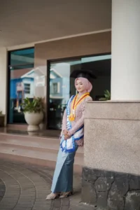 Kristina UMP, seorang mahasiswa Universitas Muhammadiyah Purwokerto, sedang berpose dalam pakaian wisuda di depan gedung.