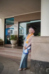 Kristina UMP, seorang wanita dalam pakaian wisuda, berpose di depan bangunan Universitas Muhammadiyah Purwokerto.