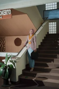 Seorang wanita dalam baju merah berdiri di atas tangga, melihat ke bawah, di Universitas Muhammadiyah Purwokerto.