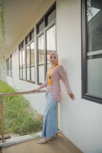 Kristina UMP, seorang wanita berpakaian merah dan putih yang berdiri di hadapan dinding, memakai celana biru dan kerudung merah.