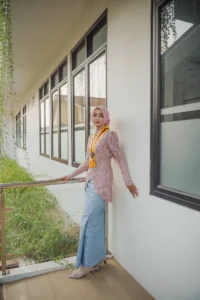 Kristina, seorang mahasiswa Universitas Muhammadiyah Purwokerto, berdiri di porche, memakai pakaian berwarna pink dan putih.