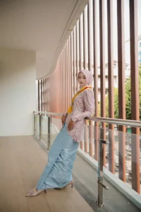 Kristina UMP universitas muhammadiyah purwokerto berdiri di atas balai dengan pakaian berwarna pink dan headscarf berwarna kuning.