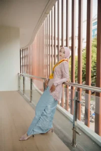 Kristina, seorang mahasiswa Universitas Muhammadiyah Purwokerto, sedang berpose di atas balai dengan pakaian berwarna merah.