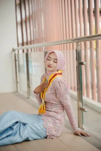 Seorang wanita berpakaian pakaian feminin sedang duduk di tanah dengan tangan di dada, wisuda Kristina dari Universitas Muhammadiyah Purwokerto.