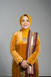 Seorang wanita dalam pakaian tradisional berdiri dengan tangan terbuka di depan tubuhnya.