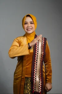 Seorang wanita berpakaian kuning dan emas sedang tersenyum dan memberikan tangan ke atas, foto ini merupakan profil kepala Kementerian Kementerian Hukum dan Hak Asasi Manusia Provinsi Purbalingga.