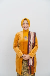 Seorang wanita dalam pakaian kuning dan oranye berdiri dan berpose untuk foto.