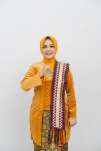 Seorang wanita dalam pakaian kuning dan oranye sedang menampilkan tanda damai.