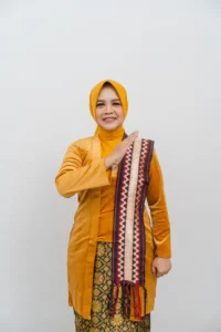 Seorang wanita berpakaian kemeja kuning sedang memegang sebuah pakaian lebar berwarna-warni.