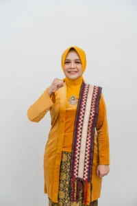 Seorang wanita berpakaian hijau memegang sepotong shawl, tersenyum dan berpose di foto profil kepala Kementerian Kebudayaan dan Pariwisata Provinsi Purbalingga.
