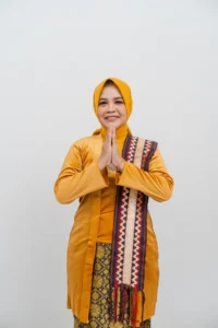 Seorang pemimpin kepala Kementerian Kebudayaan dan Pariwisata Provinsi Purbalingga berdiri dengan tangan terbuka, senyap, dalam pakaian kuning dan oranye.