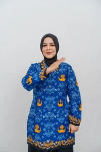 Seorang wanita berdiri dengan tangan kanan naik, memakai pakaian pola biru dan oranye.