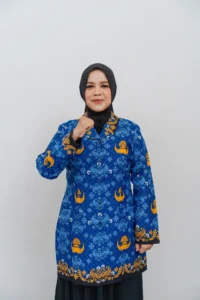 Seorang wanita berpakaian dalam pakaian biru dan emas berdiri dengan tangan terkait, foto ini merupakan profil kepala Kementerian Pendidikan dan Kebudayaan Provinsi Purbalingga.